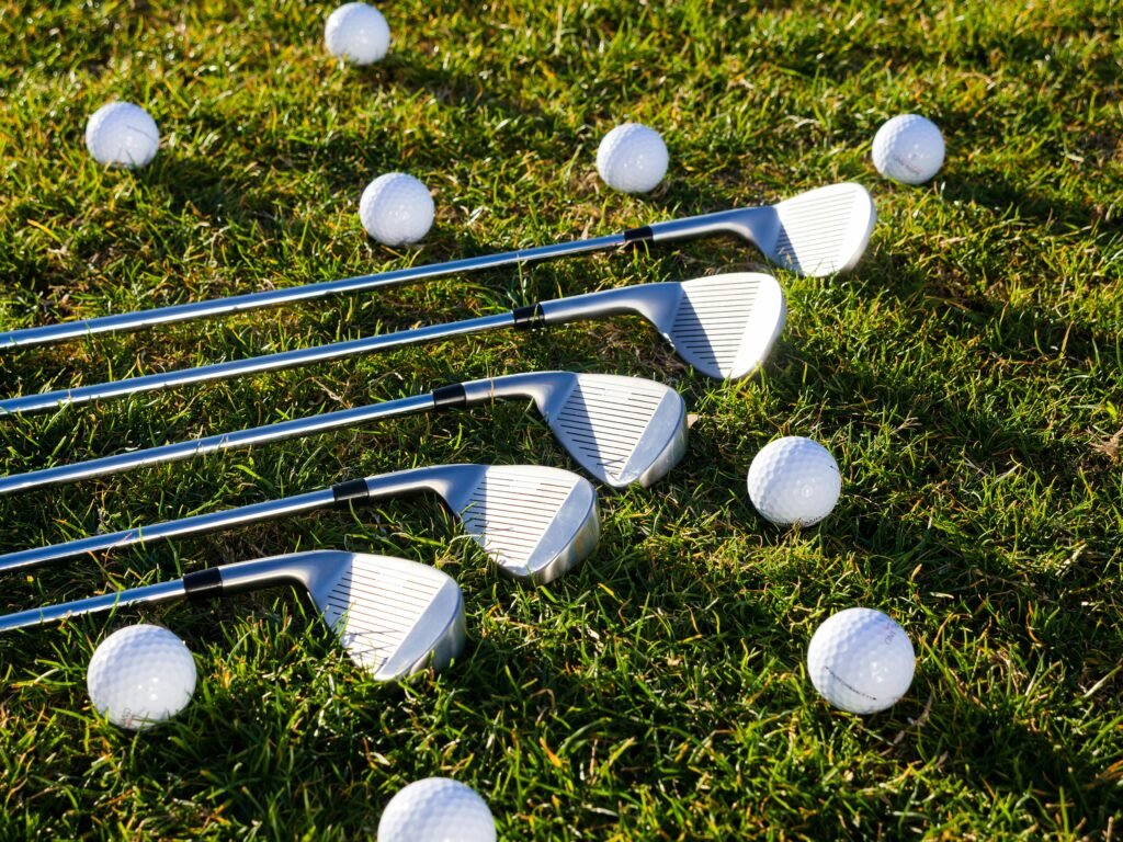 Close-up of golf clubs and balls scattered on green grass, perfect for sports equipment use.